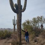 Ein junges Mädchen lehnt sich an einen großen Kaktus, im Hintergrund sieht man die Wüstenlandschaft Arizonas