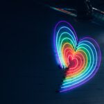 Eine Reihe von schmalen leichtenden Neonröhren auf einer Betonwand ergeben ein Herz in Regenbogenfarben.