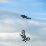 Fallschirmspringer im Sprung, unter ihm fällt sein Motorrad Richtung Boden