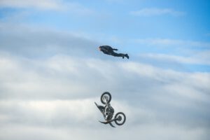 Fallschirmspringer im Sprung, unter ihm fällt sein Motorrad Richtung Boden