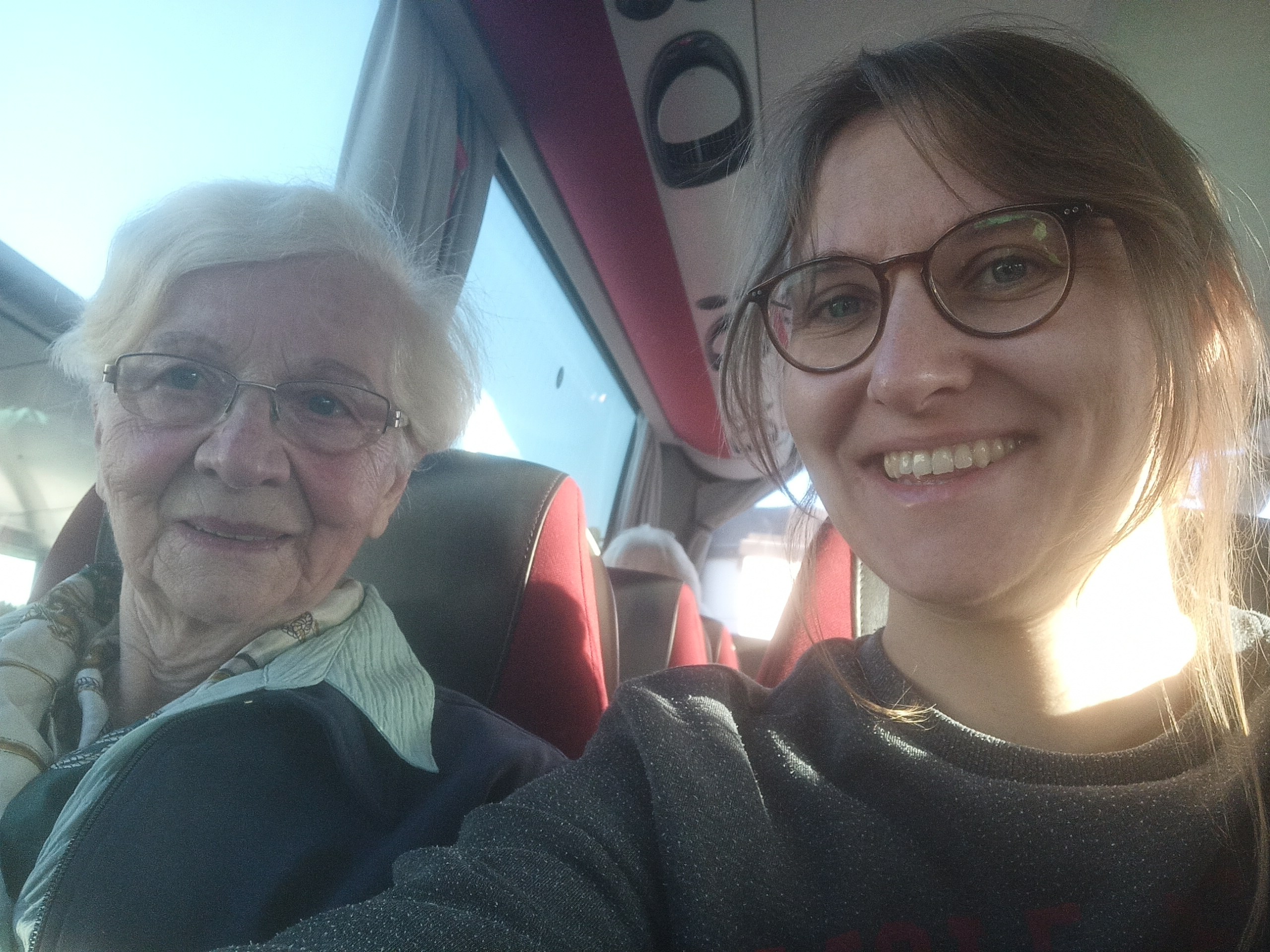 Eine Junge Frau und ihre Oma sitzen in einem Reisebus. Sie lächeln.